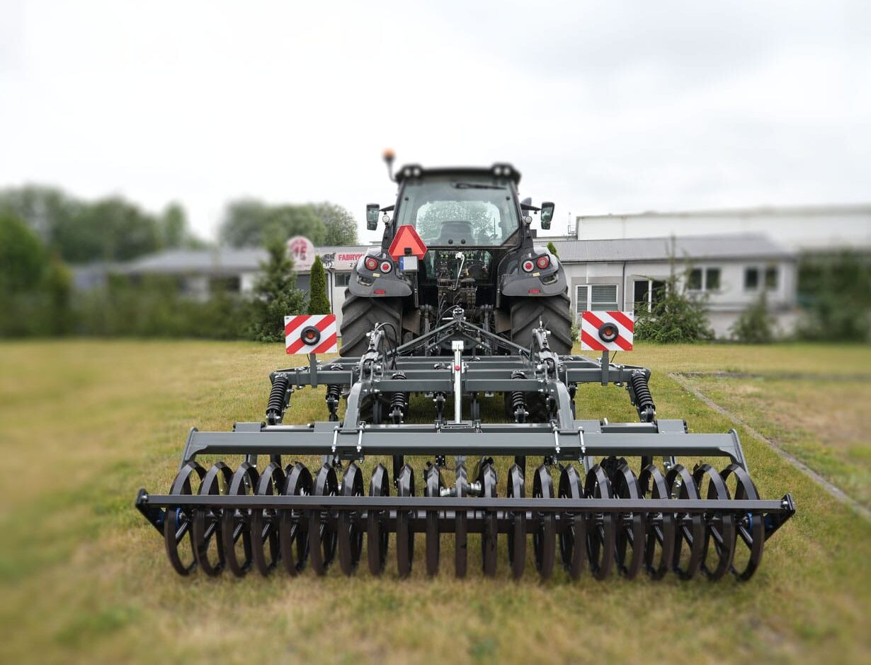 Agregat ścierniskowo-bezorkowy z kategorii: maszyny do uprawy bezorkowej AGRO-FACTYORY 2 – maszyna rolnicza podłączona do ciągnika, gotowa do pracy w polu, widok z tyłu.